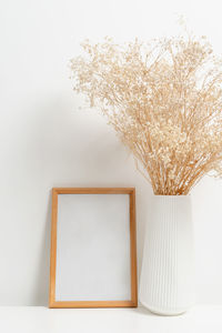 Wooden vertical frame with white vase of gypsophila flowers over white wall. mockup template 