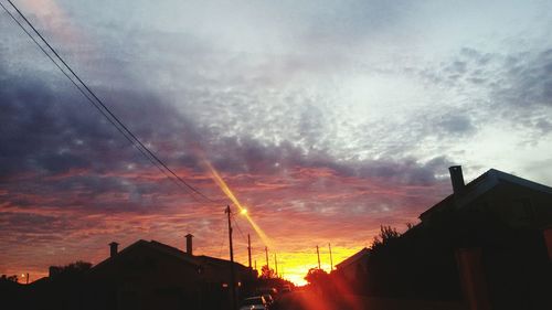 High section of silhouette houses against cloudy sky during sunset