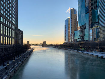 Canal amidst buildings against clear sky during sunset