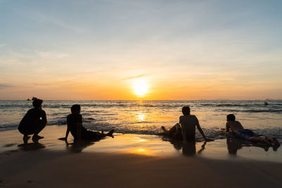 Silhouette people on beach against sky during sunset