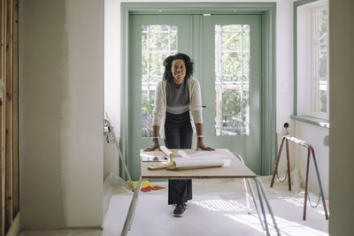 Portrait of confident female architect leaning on table at under construction apartment