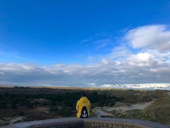 Rear view of sitting on retaining wall against cloudy sky