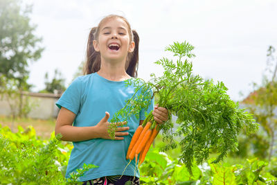 Laughing little girl in a green t-shirt holds a bunch of fresh carrots,