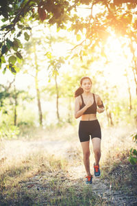 Full length of determined woman jogging on dirt road in forest