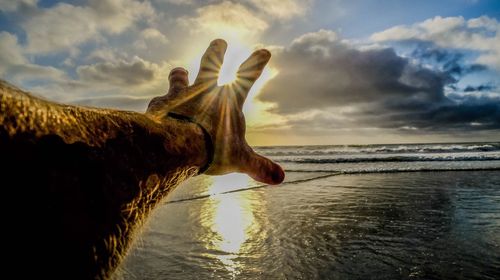 Close-up of hand on sand at beach against sky