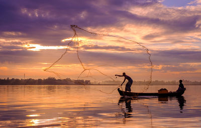 Fisherman throwing net over sea against sky during sunset