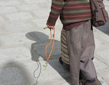 Low section of man holding religious bead on footpath