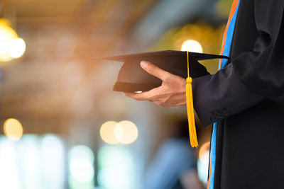 Midsection of man holding mortarboard 