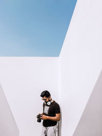 Man holding umbrella standing against white wall against clear sky