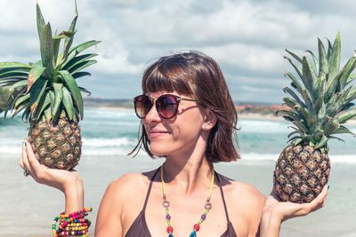 Smiling young woman holding pineapples at beach