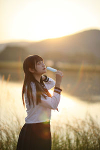 Young woman looking away while standing against sky during sunset