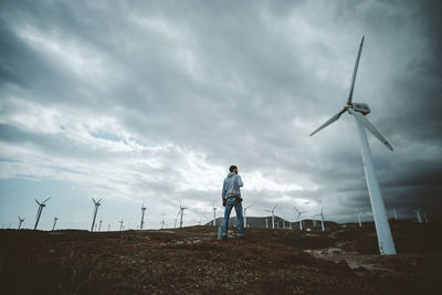 Man standing on field against wind turbines