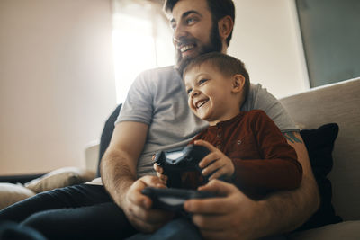 Happy father and little son sitting together on the couch playing computer game