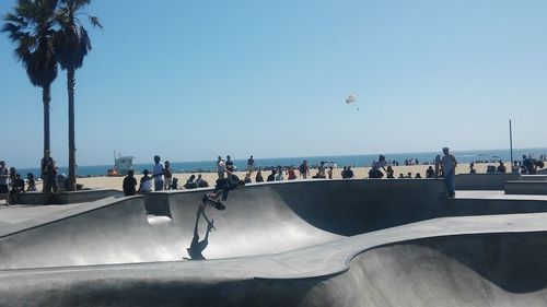 Man skateboarding at skateboard park on beach against clear blue sky during sunny day