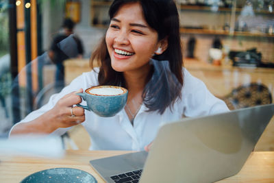 Smiling businesswoman drinking coffee while using laptop in cafe