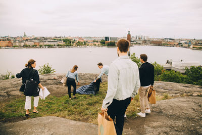 Rear view of people standing on riverbank against sky