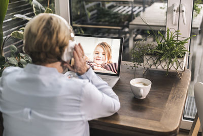 Smiling grandchild having video call with grandmother through laptop in living room