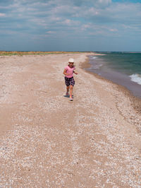 Happy child in straw hat running jumping having fun on empty autumn beach blond girl walking on sand