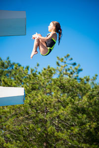 Low angle view of person jumping against clear blue sky