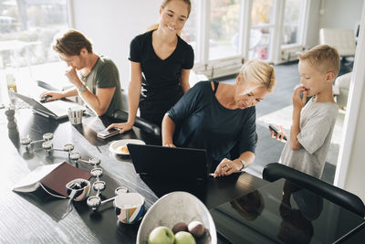High angle view of family using technologies at dining table in room