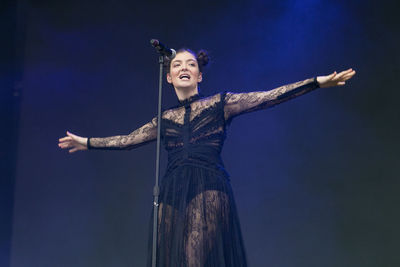 Low angle view of woman with arms outstretched against blue sky