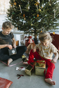 Brother and sister opening christmas presents under christmas tree  barefoot