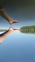 Low section of person over lake against clear blue sky