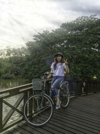 Portrait of woman showing peace sign while sitting on bicycle at bridge 