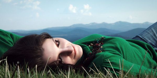 Smiling beautiful woman lying on field by mountains against sky