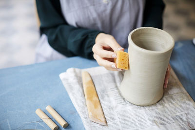 Midsection of young woman molding earthenware at table in art studio