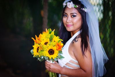 Portrait of smiling bride holding bouquet standing outdoors