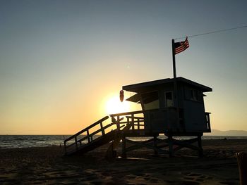 American flag on silhouette lifeguard hut at beach against clear sky during sunset