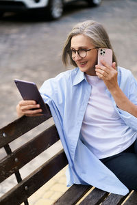 Happy senior woman is multitasking with a tablet pc and phone call on a busy city street. 