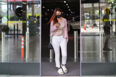 Beautiful asian women wear black mask. use mobile phone walk through glass door department stores.