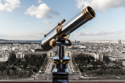 Close-up of hand-held telescope in city against sky