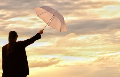 Rear view of woman holding umbrella against cloudy sky