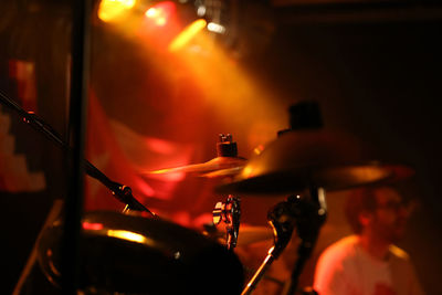Close-up of drum kit with man in background at of music concert