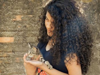 Teenage girl with curly hair holding kitten by wall