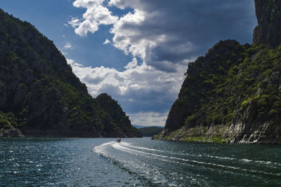 Scenic view of sea by mountain against sky