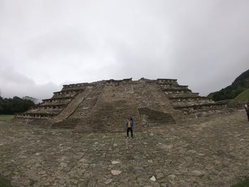 Full length of young woman standing by historical building against cloudy sky