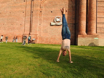Teenage boy doing handstand against brick wall on field