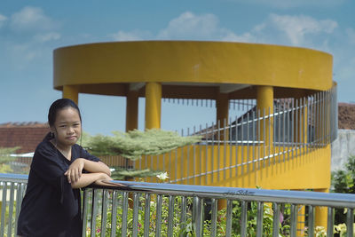 Portrait of smiling woman standing by railing against sky