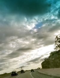 Cars on road against cloudy sky