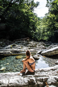 Young woman sitting on rock by river