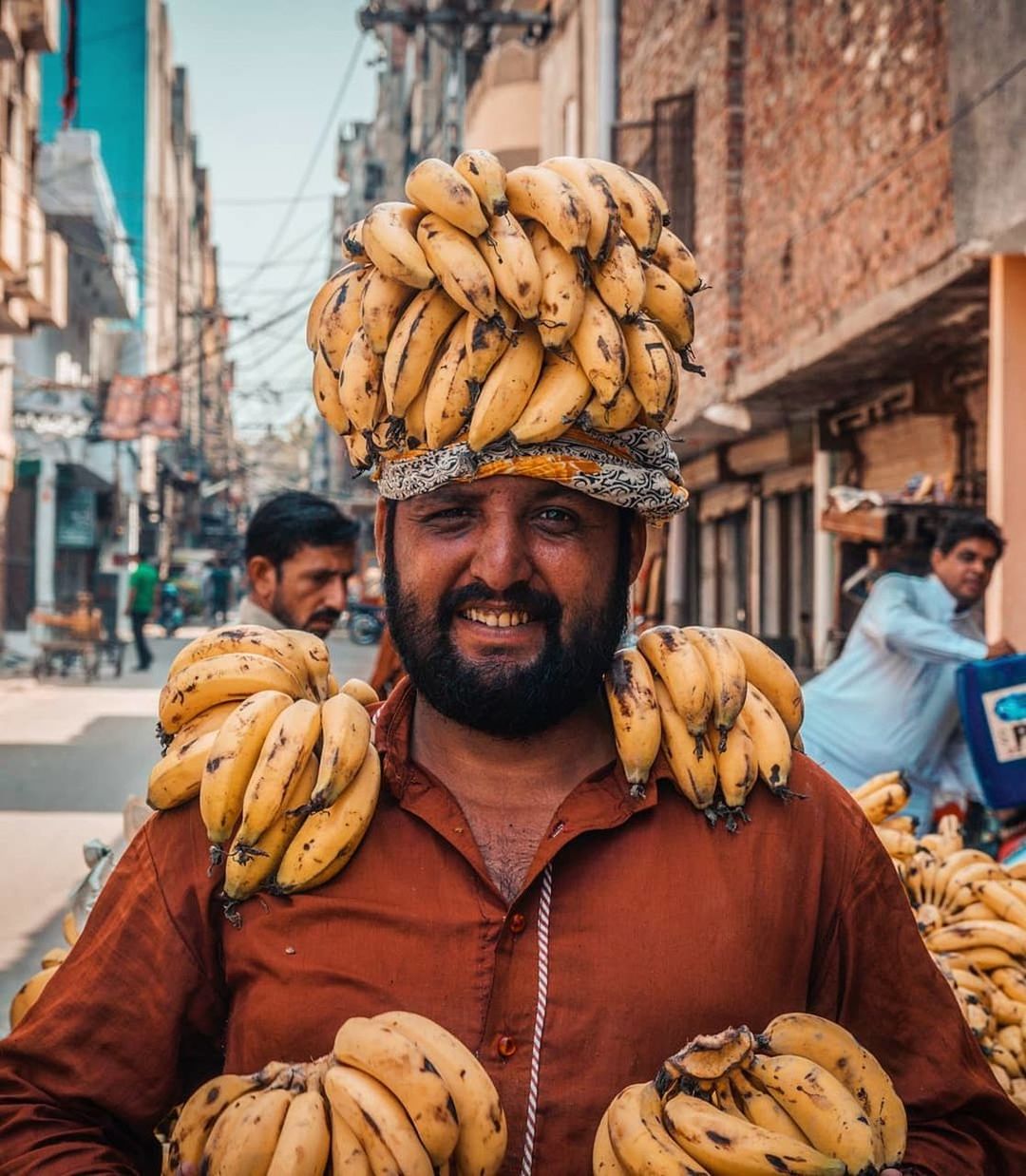 real people, beard, facial hair, front view, clothing, men, one person, focus on foreground, adult, incidental people, portrait, building exterior, traditional clothing, architecture, smiling, males, lifestyles, waist up, outdoors