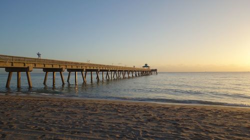 Pier over sea against clear sky during sunset