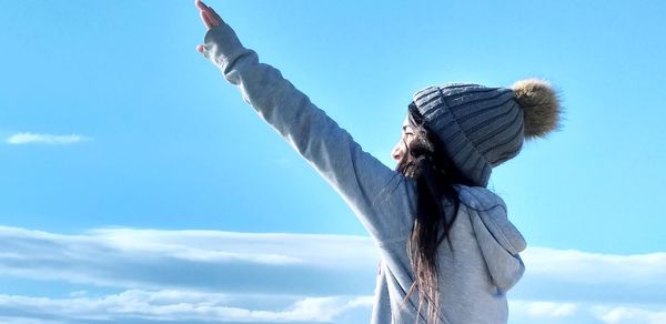 Woman with hand raised standing against blue sky