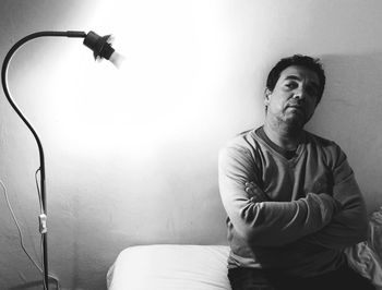 Sad man sitting by floor lamp against wall