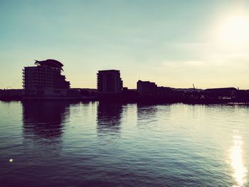 Reflection of silhouette buildings in river against sky