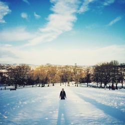 Man kneeling on snow covered field against sky